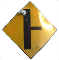 Yellow road sign with bullet hole near top corner